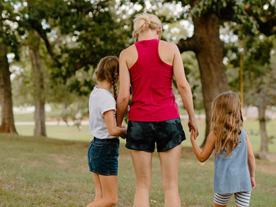 Maman de dos marchant dans un parc en tenant ses deux jeunes filles par la main