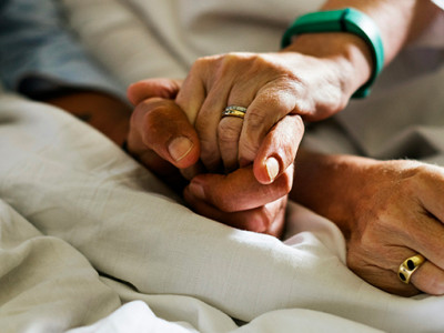 Deux mains entrelacées sur un lit d’hôpital illustrant le soutien d’une personne de confiance en fin de vie