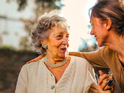 Une femme âgée souriante en discussion avec une proche bienveillante en extérieur