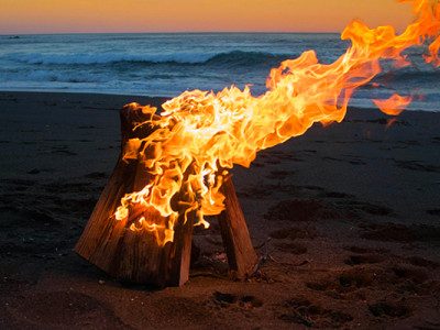 Feu de crémation symbolique sur une plage au coucher du soleil, illustrant la définition d'incinérer