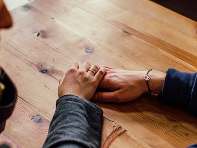 Deux personnes se tiennent la main sur une table en bois lors d’une conversation d’écoute bienveillante
