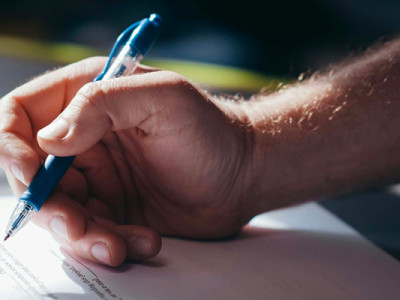 Main d’un homme en train de signer un certificat de cession après le décès du propriétaire du véhicule