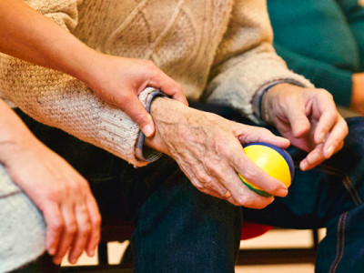 Main posée avec bienveillance sur celle d’une personne âgée tenant une balle, symbole de soutien familial.