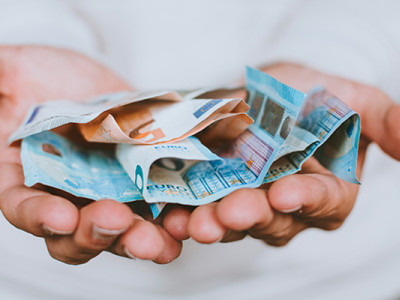 Main tendue contenant des billets d’euros, symbolisant les aides financières pour les obsèques
