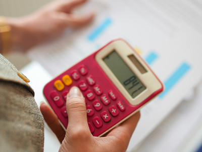 Main tenant une calculatrice rose affichant un montant, en train de vérifier une pension de réversion