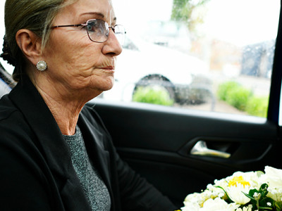 Femme âgée en deuil tenant un bouquet de fleurs dans une voiture, en route pour les obsèques