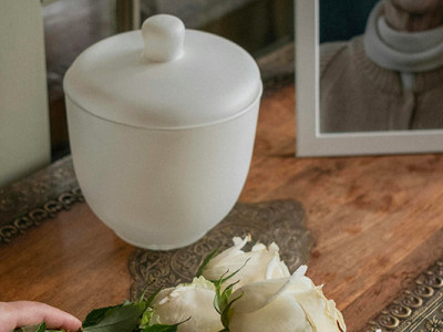 Urne funéraire blanche avec photo de la personne décédée et roses blanches après une crémation