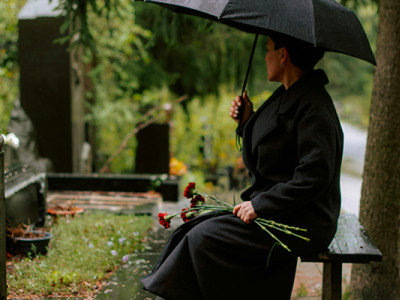 Femme assise dans un cimetière sous la pluie avec des fleurs, réflexion sur l'achat de concession funéraire