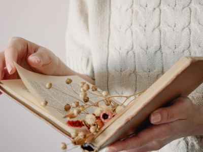 Photo d'une femme qui tient un livre ouvert avec des fleurs entre les pages du livre, symbolisant la poésie